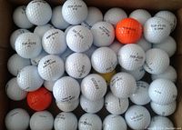 Box filled with white dimpled golf balls, mainly Top-Flite brand with XL models, some orange balls visible.