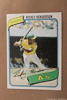 Front view of the 1980 Rickey Henderson rookie card showing Rickey Henderson swinging a bat with Oakland A's branding and his signature printed on the front.