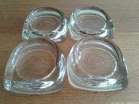 Four clear glass floor protectors placed on a wooden surface showing their flat bottom and recessed circle top areas.