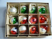 Box containing 12 vintage glass Christmas ball ornaments in individual cardboard compartments showing red, green, silver, and white colors with hand-painted and glittered designs.