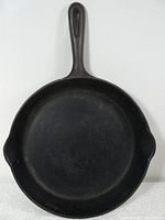 Top-down view of black cast iron frying pan showing the interior cooking surface with a handle and a pouring spout on the side.