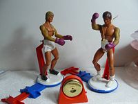 Two vintage 1971 Mattel Roundhouse Puncher male boxer action figures with gloves and championship belts, red punching indicator between them, and figure stands behind.
