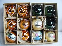 Top-down view of six divided boxes containing sets of six vintage glass Christmas ornaments each, showing various colors and hand-painted designs, packed with paper padding.