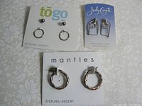 Four pairs of sterling silver earrings on three cards displayed against a light patterned background.