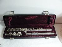 Full view of Armstrong Model 505A flute disassembled into headjoint, body, and footjoint inside open black hard case lined in burgundy velvet.
