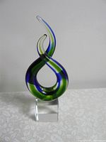 Front view showing blue and green swirls twisting in a loop on clear cube base