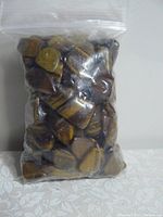Plastic bag filled with polished Tiger's Eye stones showing their characteristic golden and brown bands and glossy finish.