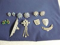 Photo showing assortment of rhinestone earrings and brooches on dark blue background.