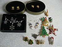 Overview of all Christmas themed jewelry items including pins, earrings and necklace shown on a light surface.