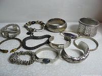 Full lot of eleven silver-toned costume bracelets displayed on a flat surface showing various bracelet styles and sizes.