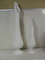 Pair of white hobnail milk glass vases with ruffled tops on a light patterned surface.