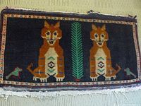 Handwoven mat showing two orange foxes on dark background with central green motif and patterned border.