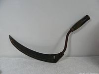 Full view of an antique sickle with curved rusted metal blade and wooden handle.