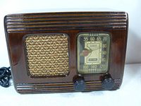 Front view of small vintage RCA wooden radio showing speaker grille, tuning dial, and two control knobs.