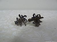Pair of sterling silver cufflinks with Chinese character design shown from front angle on white patterned background.