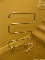 Full view of chrome towel warmer rack with serpentine bar design, power cord on the floor.