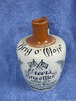 Front view of vintage ceramic whisky bottle with printed text 'Brig o' Weir Greer's Rare Old Liqueur Whisky Wm Greer & Co Ltd Glasgow' and crossed flags design.