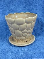Side view of the vintage McCoy planter showing the pale peach glaze and honeycomb textured exterior with scalloped rim and attached saucer base with drainage hole.