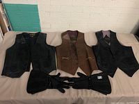 Three leather vests and one pair of black motorcycle gloves displayed on a table.