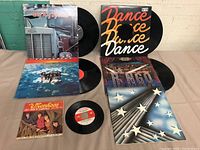 Five LP albums and one 45rpm single displayed on a table showing album covers and records partly out of sleeves.