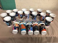 Photo showing 16 McDonald's collectible cups featuring Batman and other character designs, arranged on a table.