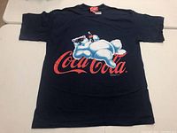 Full front view of black vintage Coca-Cola T-shirt showing polar bear graphic and Coca-Cola logo.