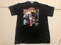 Front view of black T-shirt with large colorful graphic showing a woman reaching up to a man sitting in a blue truck cab with text around the image.