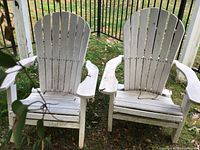 Front view of both Adirondack chairs side by side on grass with metal fence background