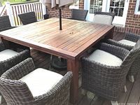 Overview of eight brown wicker chairs with light fabric cushions arranged around a large wood table on a deck