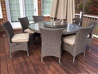 Full view of all eight wicker chairs arranged around a glass-top table on a deck