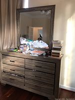 Woodgrain dresser with mirror on top and multiple personal items placed on dresser surface.