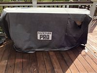 Grill covered by Backyard Pro fabric cover showing tear on right side