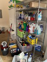 Wide view of metal shelving with various cleaning chemicals, detergents, and supplies including mop and pail, vacuum bags, and assorted spray bottles and containers.
