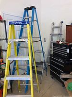 Yellow Werner 6-ft fiberglass step ladder, blue Werner 8-ft step ladder, two-step stool, and folded multi-position ladder shown in garage