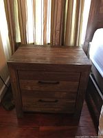 Front view of one nightstand showing two drawers and metal handles, rustic dark wood finish.