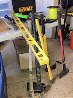 Photo showing a collection of tools leaning against a table including axes, sledge hammer, level, and DeWalt case