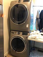 Washer and dryer stacked one atop the other in a room corner with table and clothes nearby
