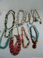Overall lot of more than 12 decorative necklaces showing a variety of styles and materials on a white background.