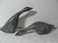 Pair of soapstone bird sculptures on a fabric surface with plain off-white background, showing side profiles and overall shape.