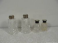 Front view of both pairs of shakers showing cut glass pattern and sterling silver tops on the larger pair alongside smaller pair with dark metal tops.