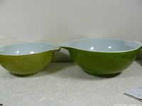Two vintage Pyrex mixing bowls side by side, showing different shades of green exterior and white interior.