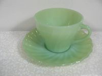 Side angled view of the green Jadite glass cup and saucer displaying the swirl pattern and overall shape.