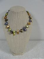 Antique multicoloured baroque pearl necklace displayed on a beige jewellery bust.