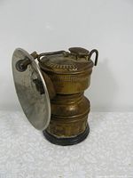 Side view of the brass carbide miner's lamp showing the reflector dish and top lid with embossed markings.