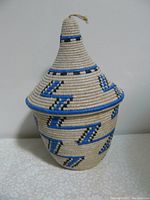 Front angle showing the conical lidded basket with blue, black, and white zigzag patterns and loop handle on lid