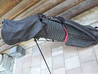 Black golf bag with shoulder strap and stand, showing Zip pockets and padded texture