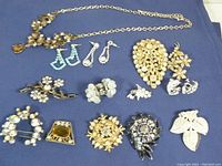 Full layout of all jewelry items on blue cloth showing variety including necklace, earrings, and brooches.