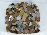 Top view of a large pile of assorted foreign coins in a white container showing various sizes and colors.