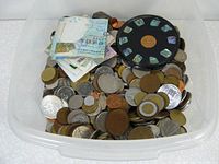 Top view showcasing the plastic tub filled with a large number of coins, some folded banknotes, and a circular object.