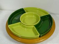 Top-down view of the assembled lazy Susan server showing the wooden base and five ceramic dishes in shades of green arranged circularly.